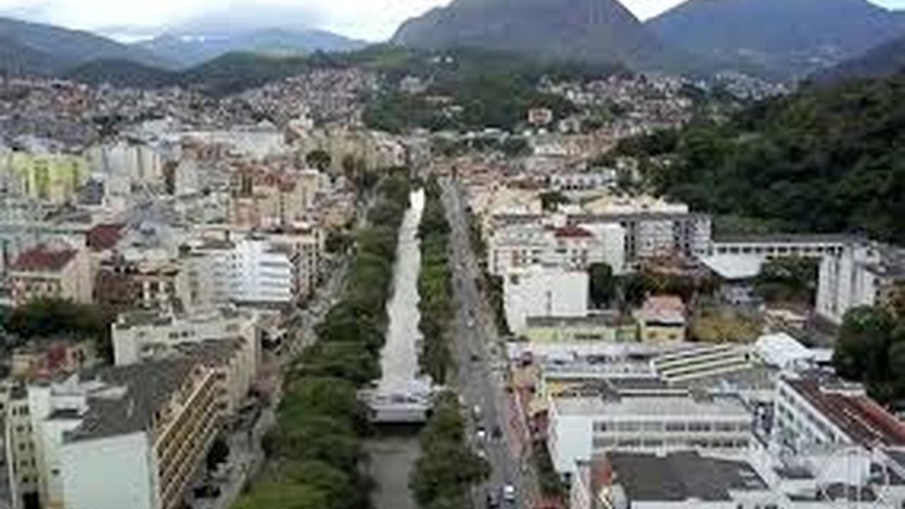Vista aérea de Nova Friburgo, cidade na região serrana do Rio de Janeiro, com montanhas ao fundo e rio no meio.