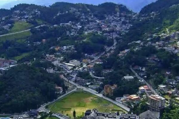 Vista aérea de uma cidade montanhosa com casas e ruas sinuosas, com foco na área de Quitandinha, Petrópolis, onde moradores relatam ter sentido tremores.