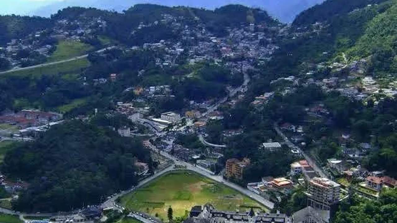 Vista aérea de uma cidade montanhosa com casas e ruas sinuosas, com foco na área de Quitandinha, Petrópolis, onde moradores relatam ter sentido tremores.