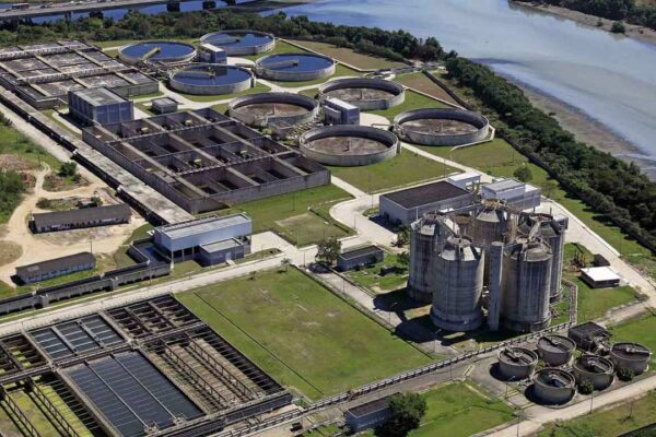 Vista aérea de uma estação de tratamento de água com tanques circulares, filtros retangulares e silos altos, indicando uma grande estrutura de tratamento de água.