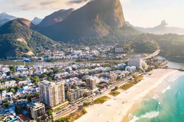 Vista aérea de uma praia no Rio de Janeiro, com edifícios, montanhas e mar azul.