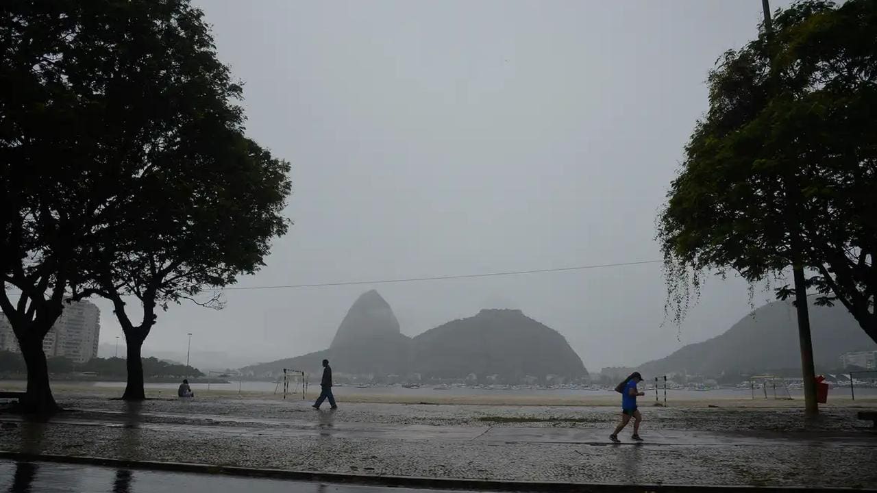 Vista chuvosa do Rio de Janeiro, com pessoas caminhando e montanhas ao fundo.