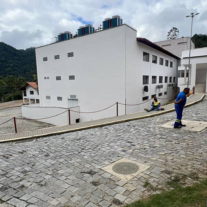Vista externa do Hospital do Câncer de Nova Friburgo em construção, mostrando um pátio com piso de paralelepípedos.