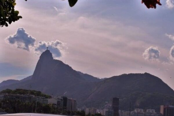 Vista panorâmica da cidade do Rio de Janeiro com o Cristo Redentor no topo do Morro do Corcovado, sob um céu nublado com a promessa de chuva, mas ainda com sol