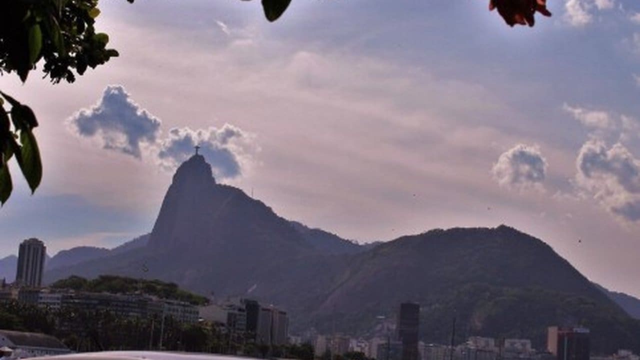 Vista panorâmica da cidade do Rio de Janeiro com o Cristo Redentor no topo do Morro do Corcovado, sob um céu nublado com a promessa de chuva, mas ainda com sol