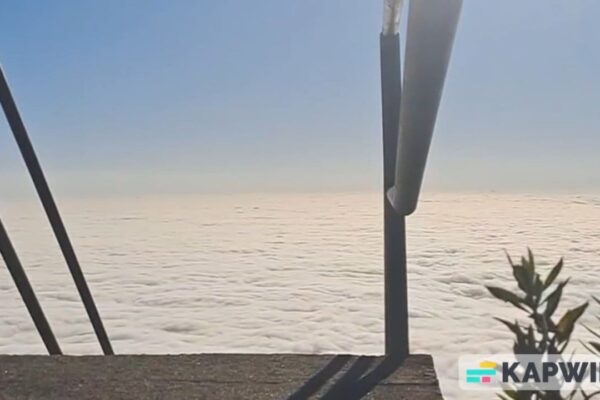 Vista panorâmica do mar de nuvens em Nova Friburgo, com céu azul e estrutura metálica em primeiro plano.