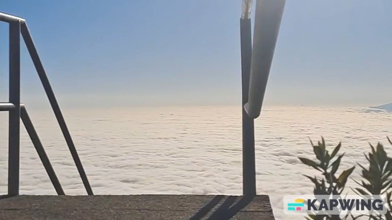 Vista panorâmica do mar de nuvens em Nova Friburgo, com céu azul e estrutura metálica em primeiro plano.