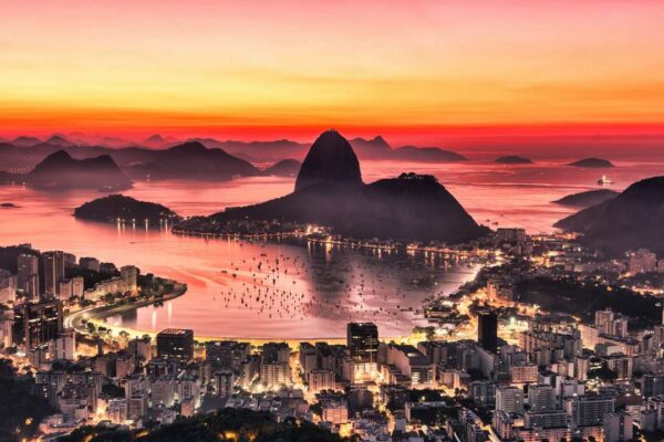 Vista panorâmica do Rio de Janeiro ao pôr do sol, com montanhas e cidade iluminada.