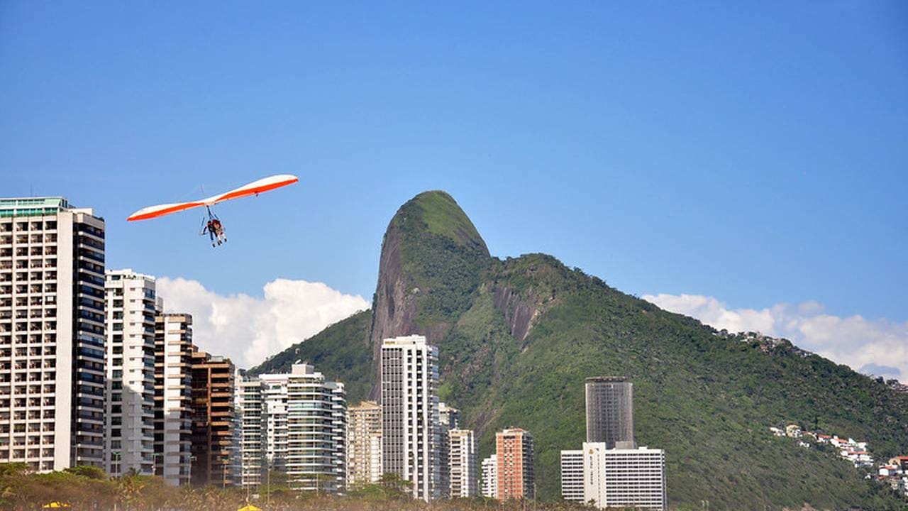 Voo de parapente sobre o Rio de Janeiro, com montanha e prédios ao fundo