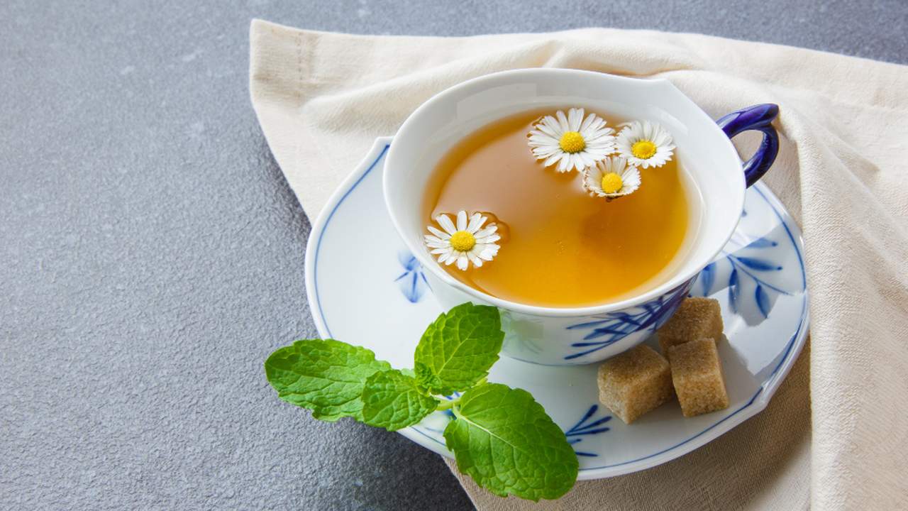 Xícara de chá de camomila com flores, acompanhada de açúcar e hortelã fresca.
