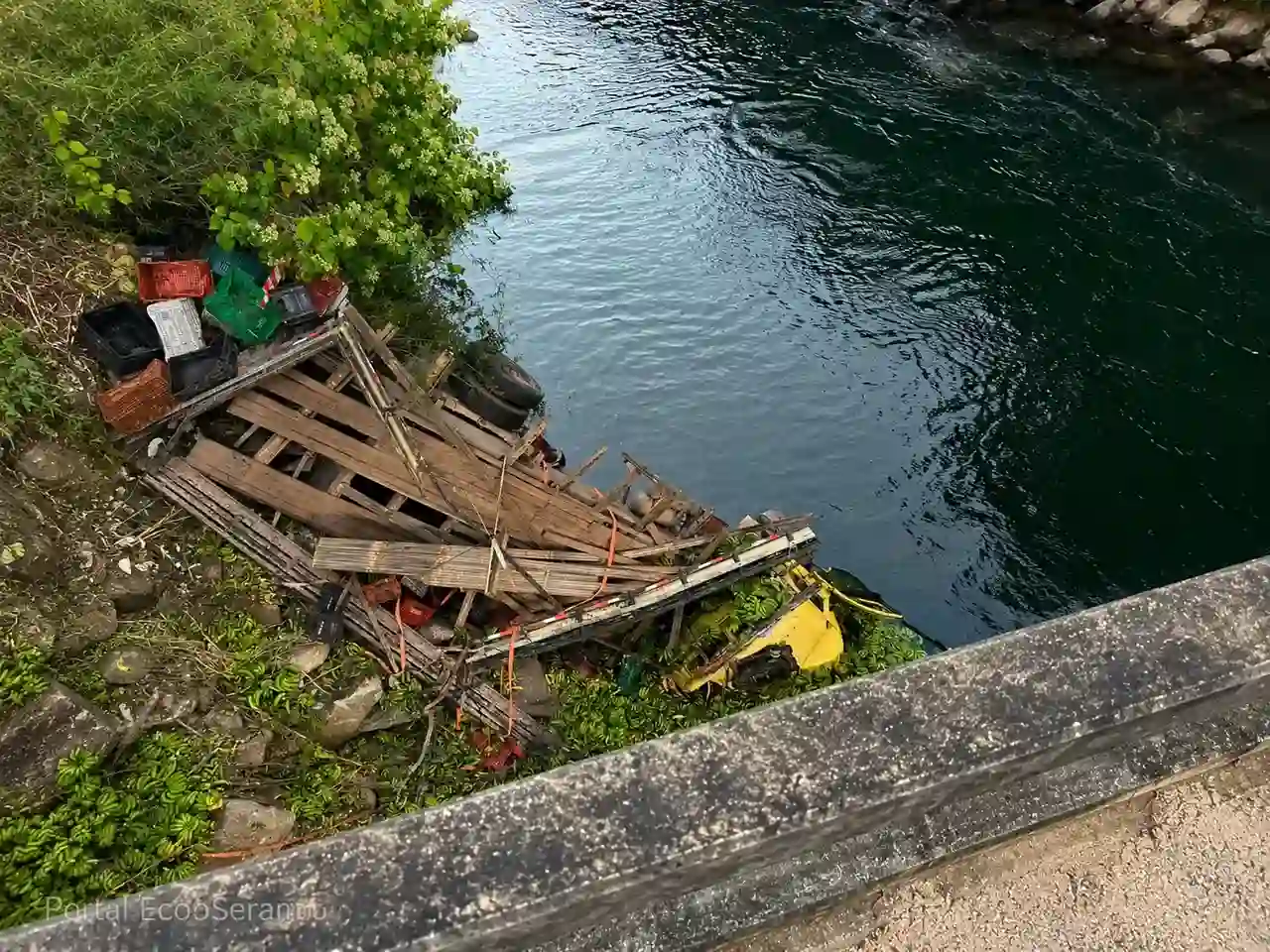Caminhão destruído às margens do rio após sair da pista na RJ-142, próximo à Ponte de Santa Luzia.