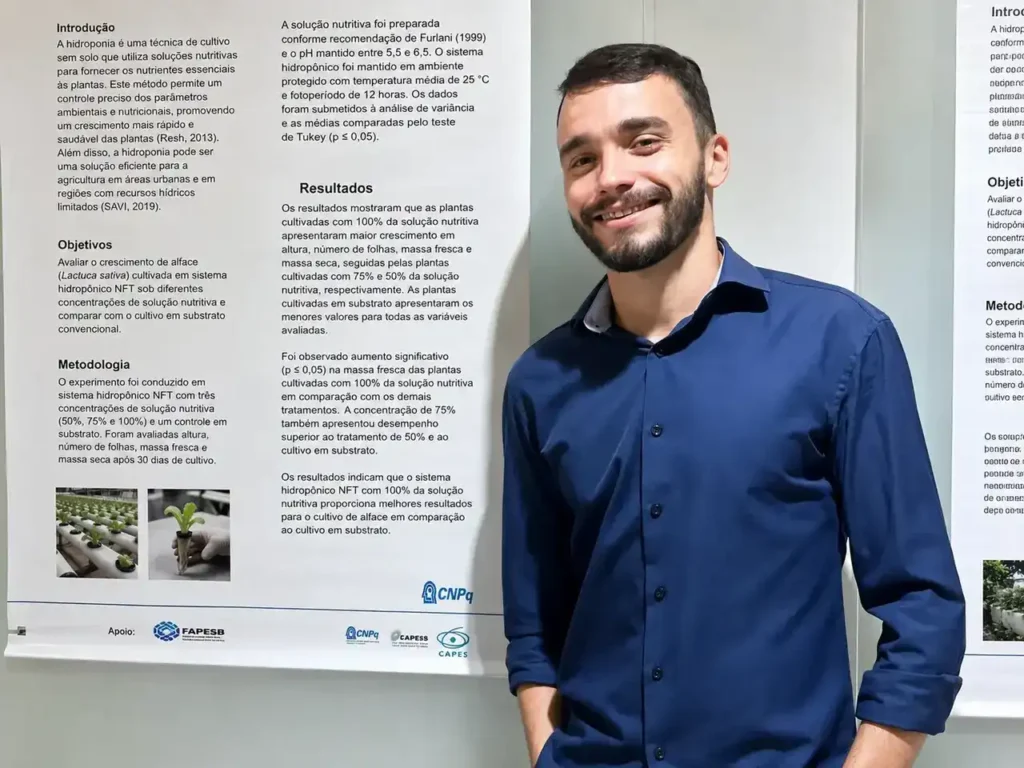 Gabriel Serra posa em frente a um pôster acadêmico em ambiente interno.
