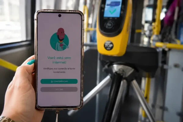 Passageiro utiliza o aplicativo Jaé no celular diante de um validador do transporte público do Rio.