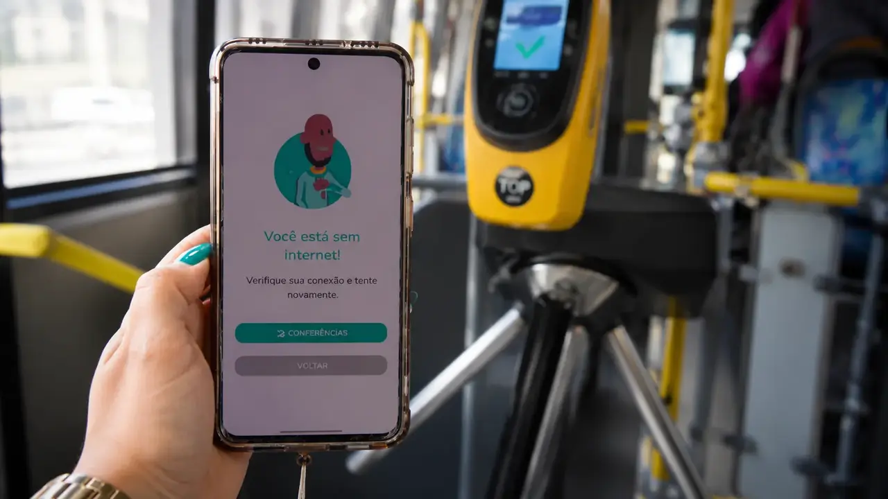 Passageiro utiliza o aplicativo Jaé no celular diante de um validador do transporte público do Rio.
