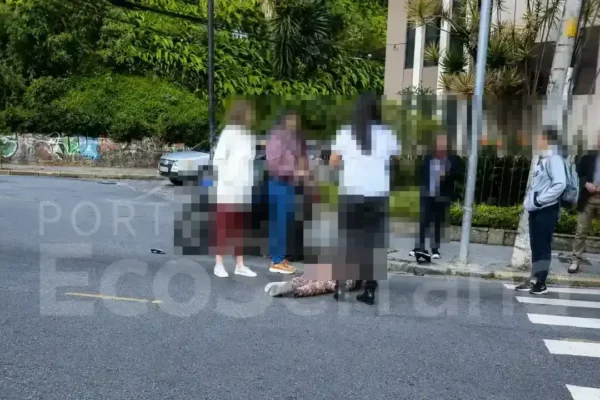 Pessoas ao redor de uma vítima caída na pista após atropelamento em cruzamento urbano de Nova Friburgo.
