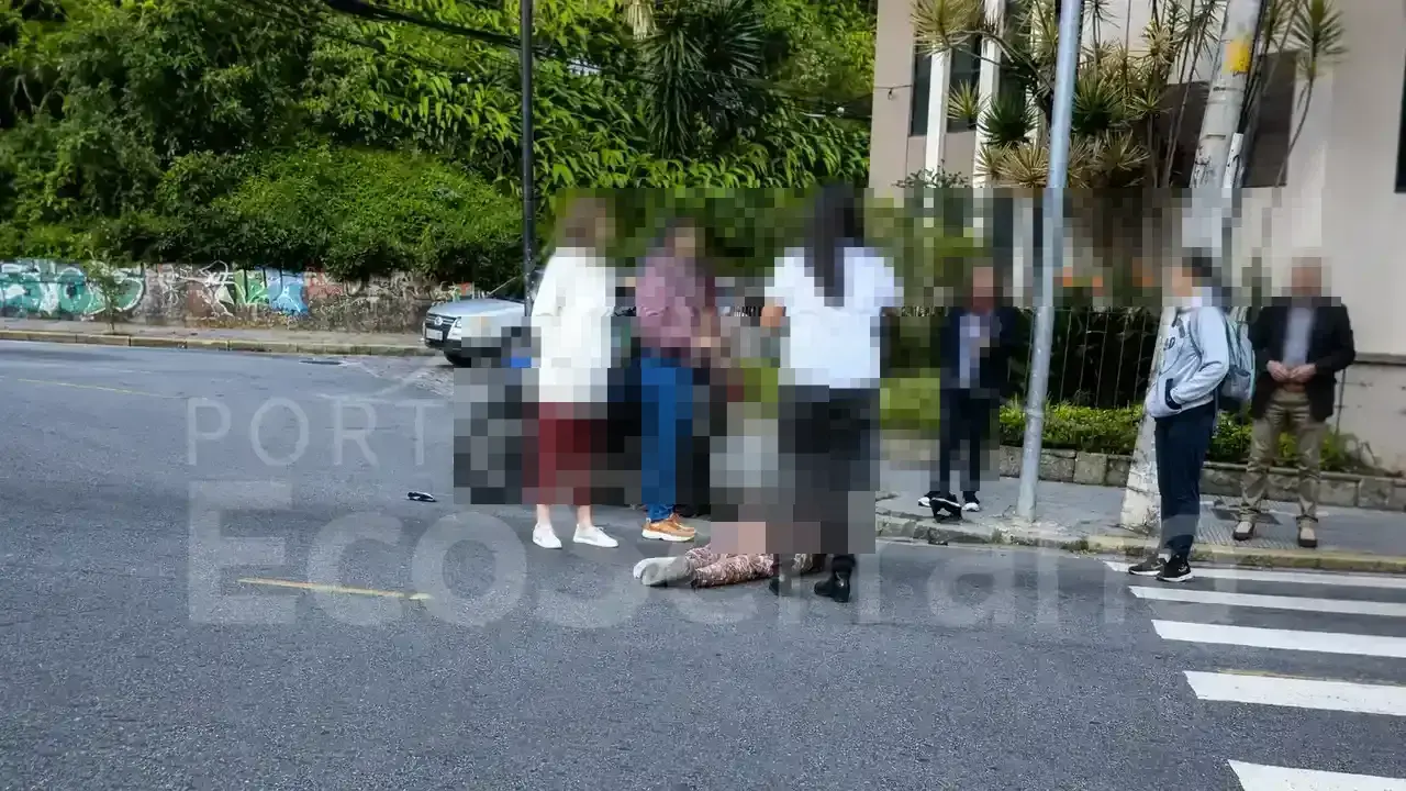 Pessoas ao redor de uma vítima caída na pista após atropelamento em cruzamento urbano de Nova Friburgo.