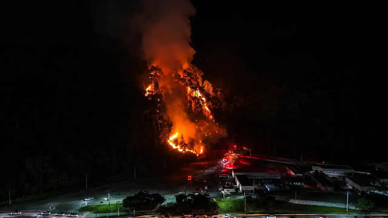 Incêndio em área de vegetação durante a noite em Olaria, Nova Friburgo, com chamas próximas a estruturas da Unidos do Imperador.