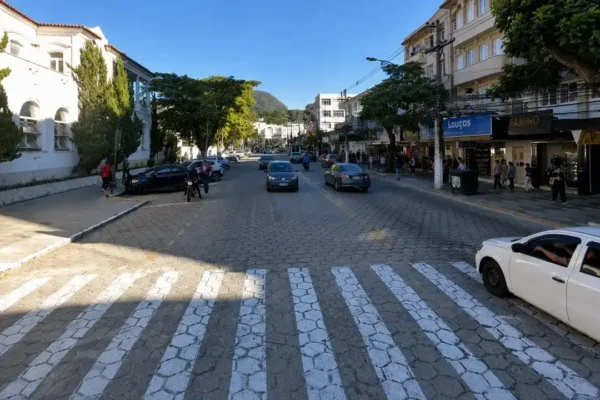 Imagem do Google Maps mostra trecho da Avenida Alberto Braune, no Centro de Nova Friburgo, com carros circulando, comércio aberto, calçadas movimentadas e prédios nos dois lados da via.