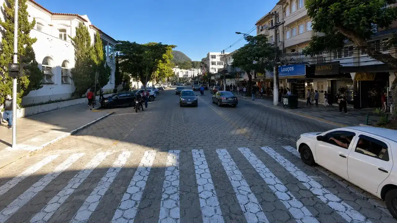 Imagem do Google Maps mostra trecho da Avenida Alberto Braune, no Centro de Nova Friburgo, com carros circulando, comércio aberto, calçadas movimentadas e prédios nos dois lados da via.