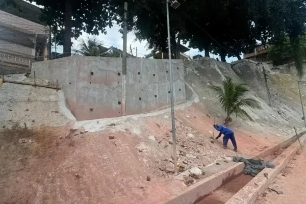Obra de contenção de encosta no Parque Muísa, em Duque de Caxias, com muro de estabilização, área em recuperação e trabalhador no local.