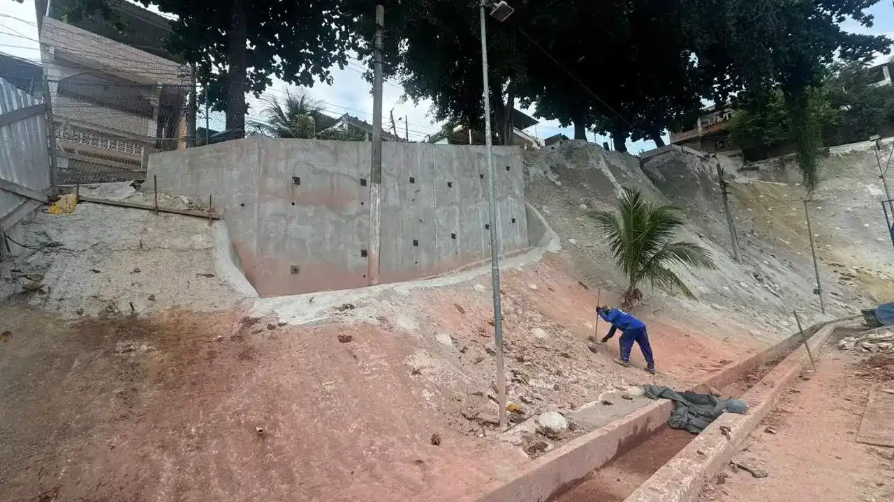 Obra de contenção de encosta no Parque Muísa, em Duque de Caxias, com muro de estabilização, área em recuperação e trabalhador no local.