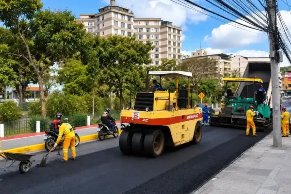 Máquinas e equipes trabalham no recapeamento da RJ-116 enquanto veículos passam pelo sistema Pare e Siga no bairro Paissandu, em Nova Friburgo.