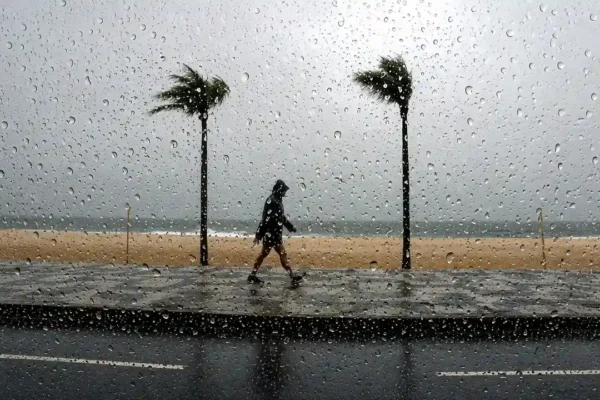 Pessoa caminha pela orla durante chuva vista através de vidro molhado