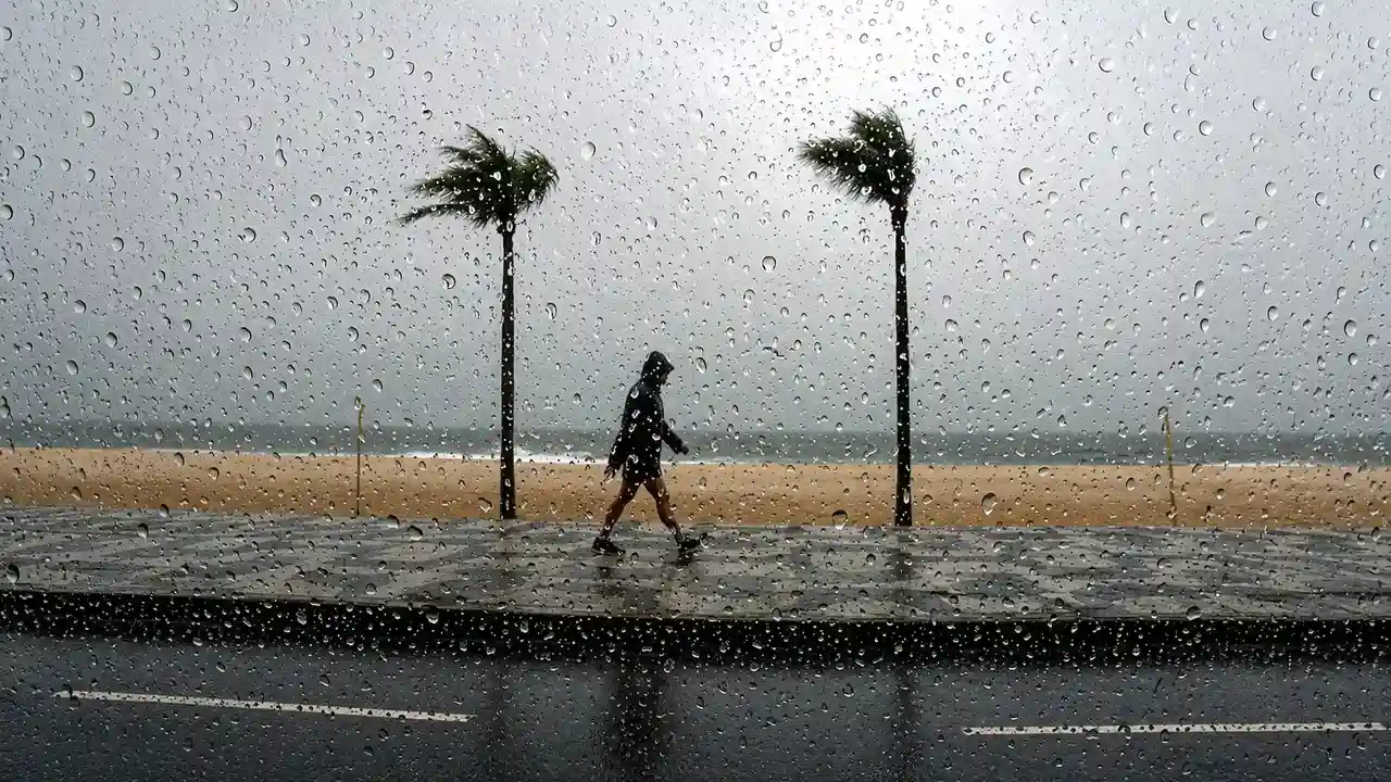 Pessoa caminha pela orla durante chuva vista através de vidro molhado