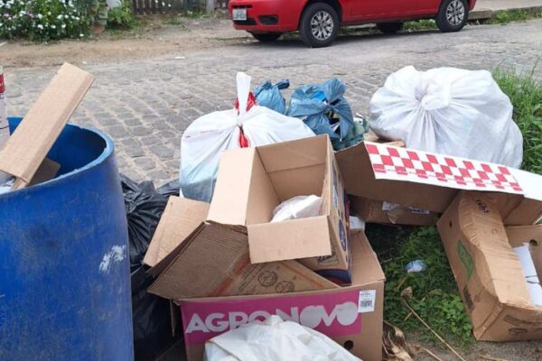 Acúmulo de lixo na rua, com caixas de papelão, sacos plásticos e um tambor azul.