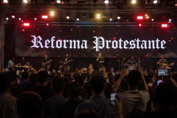 Banda se apresentando no evento Reforma Protestante com a palavra 'Reforma Protestante' no telão.