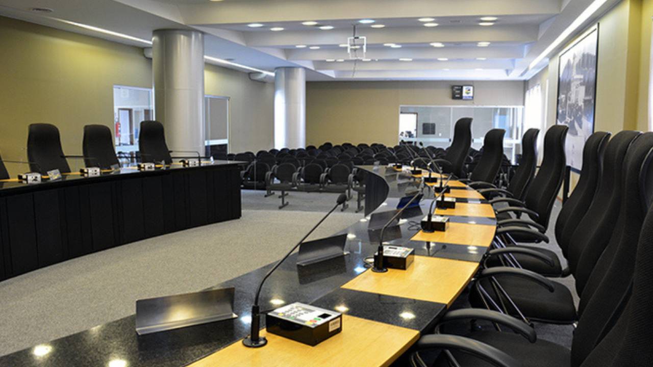 Câmara municipal com cadeiras e mesa para reuniões.