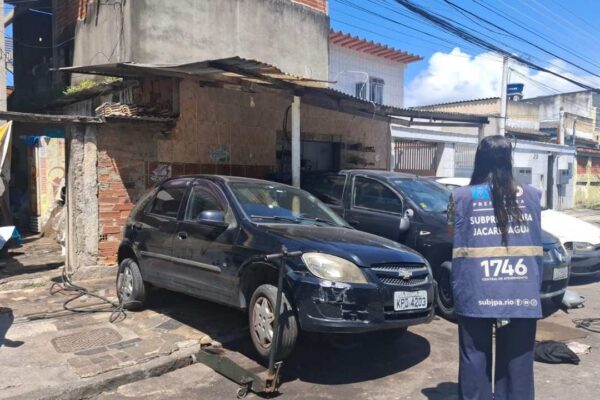 Carro preto em oficina interditada, com policial em ação