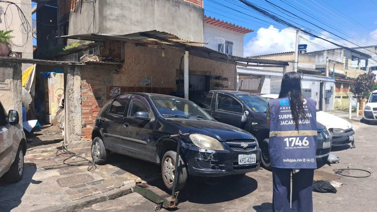 Carro preto em oficina interditada, com policial em ação