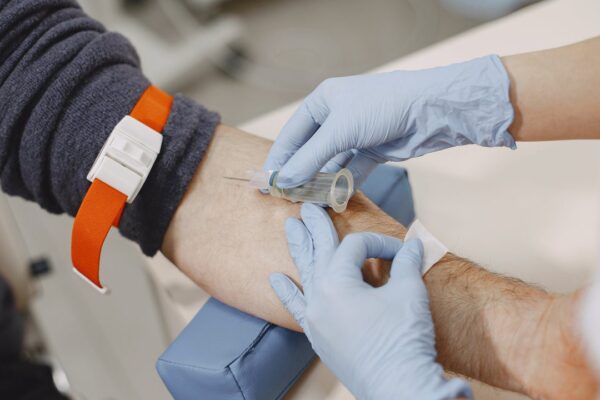 Coleta de sangue em paciente hospitalizado com torniquete no braço e luvas.