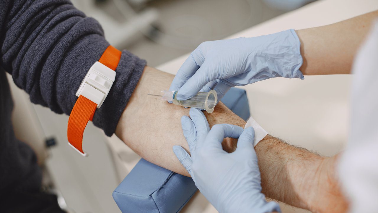 Coleta de sangue em paciente hospitalizado com torniquete no braço e luvas.