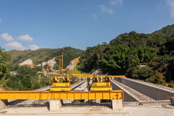 Construção de ponte em região montanhosa com equipamentos e natureza ao fundo.