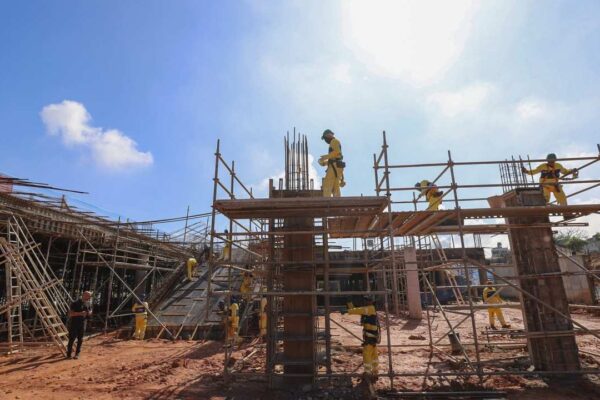 Construção do terminal BRT em Santa Cruz, com operários trabalhando na obra sob céu azul.