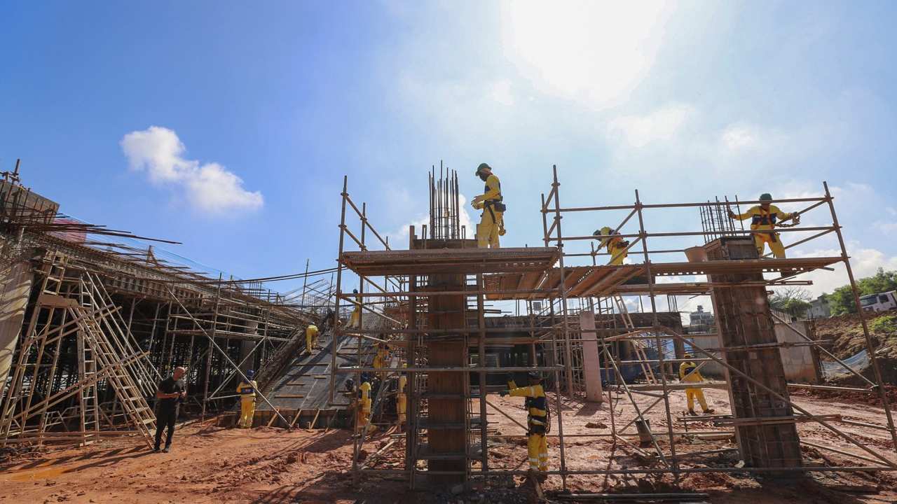 Construção do terminal BRT em Santa Cruz, com operários trabalhando na obra sob céu azul.