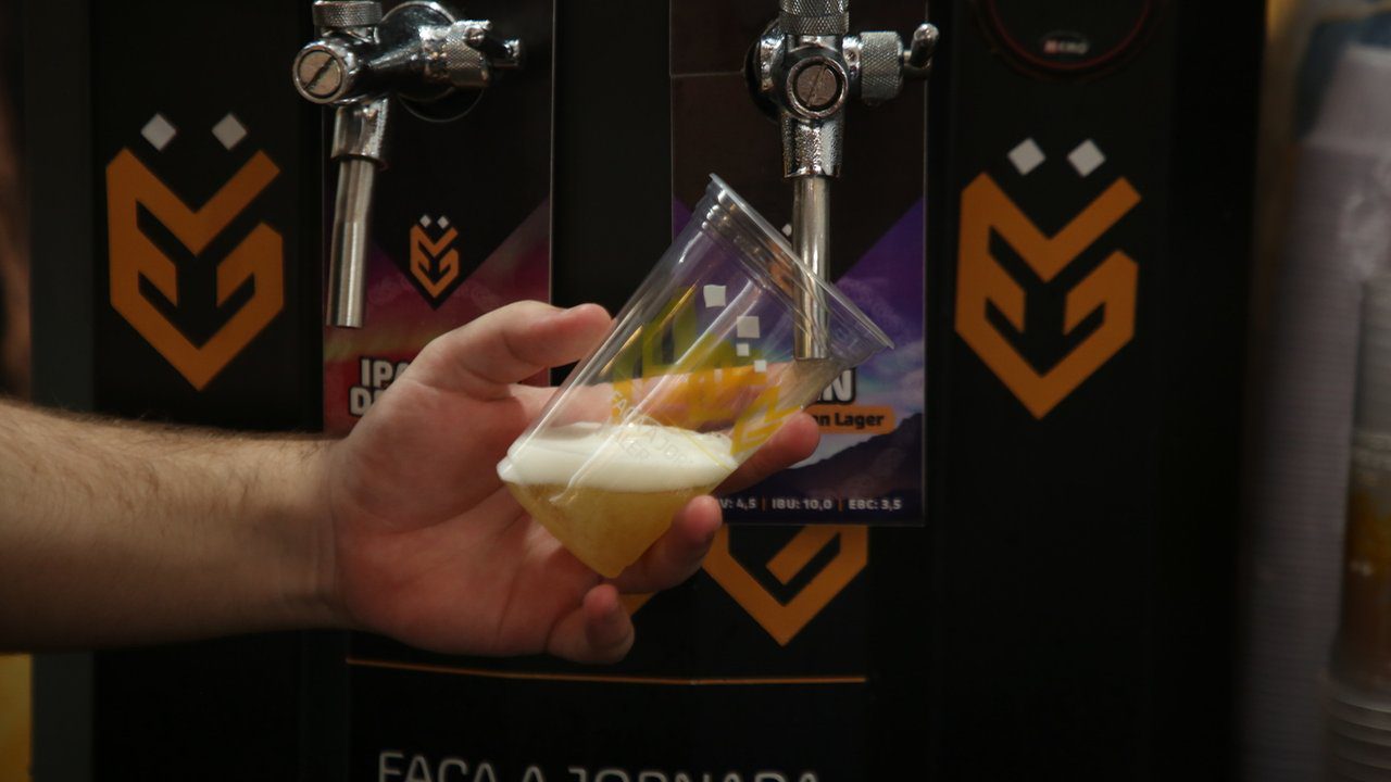 Copo de cerveja sendo servido em evento de cervejas artesanais. Foco na espuma e no líquido.