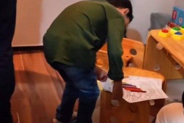 Criança atípica em atividade em espaço de apoio familiar, com desenho e lápis de cor.