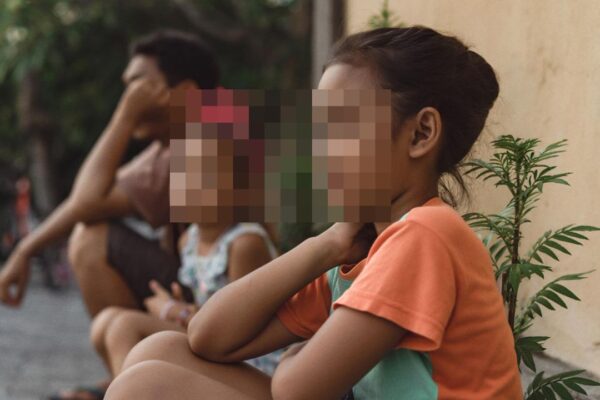 Crianças e adulto sentados, imagem pixelada, contexto de problemas estruturais e excesso de acolhidos.