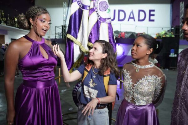 Entrevista com participantes do desfile de escolas de samba, com pessoas vestidas em trajes elaborados.