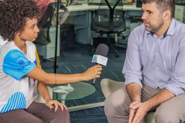 Entrevistadora com microfone entrevista homem em ambiente de escritório.