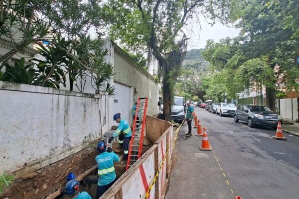 Equipe da concessionária CG Rio realiza manutenção em rua, com vala aberta e cones de sinalização.