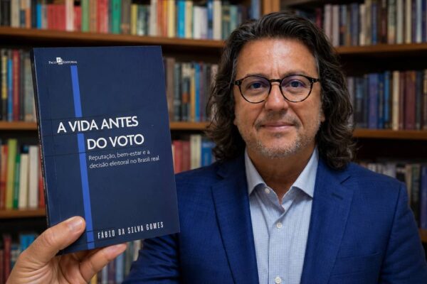 Sociólogo Fábio Gomes apresenta o livro “A Vida Antes do Voto” diante de uma estante de livros.