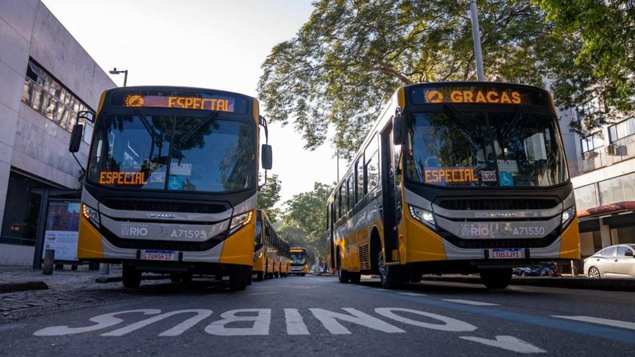 Dois ônibus novos do Sistema RIO estacionados em uma via urbana, com outros veículos ao fundo, durante apresentação da nova frota municipal.