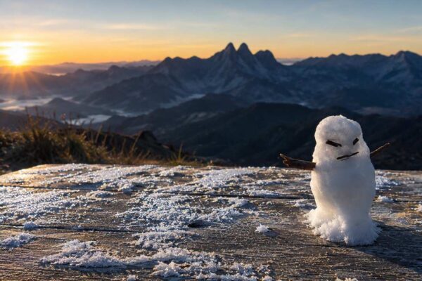 Boneco de gelo sobre uma superfície coberta por geada ao amanhecer, com arte destacando as temperaturas mínimas registradas em Nova Friburgo, Itatiaia e outras cidades do Estado do Rio de Janeiro.