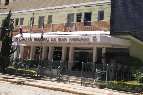 Fachada da Câmara Municipal de Nova Friburgo, com bandeiras e grade de proteção.
