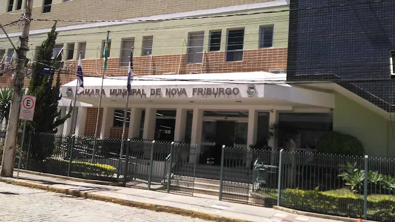 Fachada da Câmara Municipal de Nova Friburgo, com bandeiras e grade de proteção.