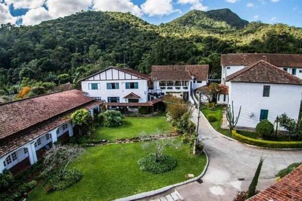 Fachada do Hotel Buscky, com edifícios brancos e telhados de telha, em meio à natureza.